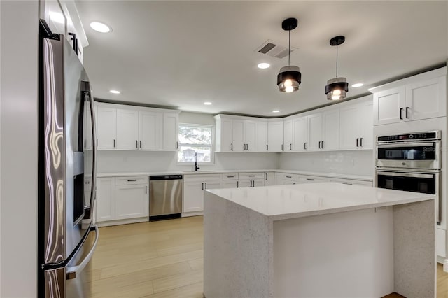 10744 Drummond Rd, Tampa, FL 33615 - kitchen featuring appliances with stainless steel finishes, a kitchen island, light wood-type flooring, pendant lighting, and white cabinets