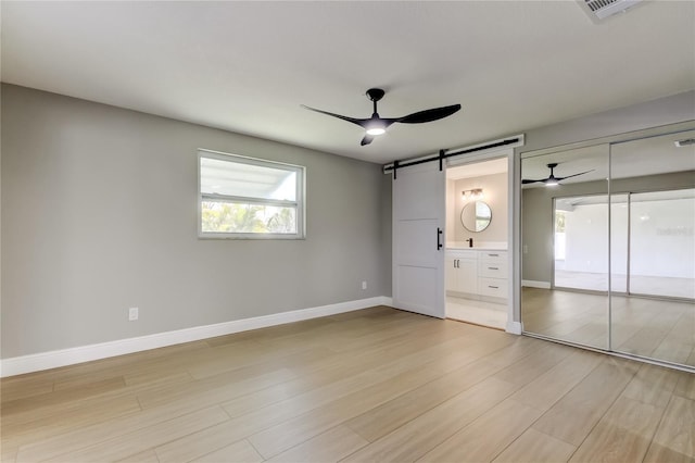 10744 Drummond Rd, Tampa, FL 33615 - unfurnished bedroom featuring a barn door, light wood-style floors, baseboards, and ensuite bathroom
