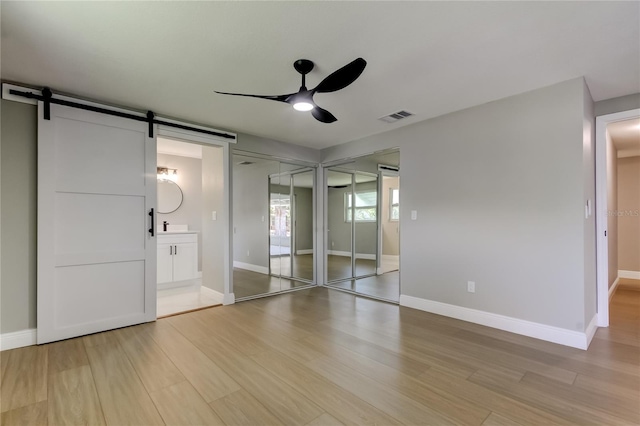 10744 Drummond Rd, Tampa, FL 33615 - unfurnished bedroom featuring a barn door, light wood-type flooring, and baseboards