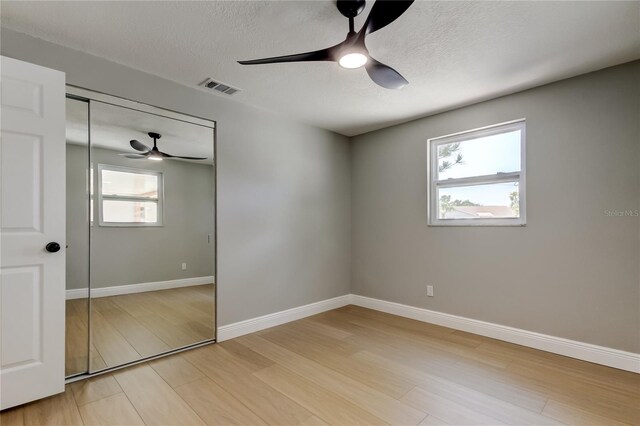 10744 Drummond Rd, Tampa, FL 33615 - unfurnished bedroom with multiple windows, light wood-style floors, a closet, baseboards, and a textured ceiling