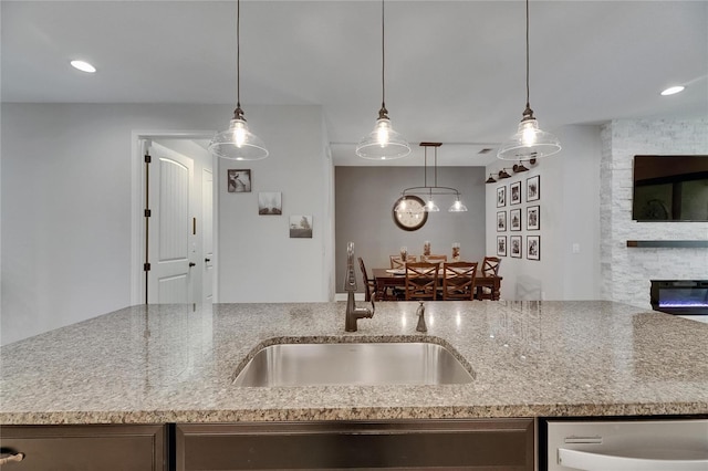 12957 Satin Lily Dr, Riverview, FL 33579 - kitchen with a sink, stainless steel dishwasher, light stone counters, a fireplace, and hanging light fixtures