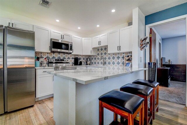 4050 4th St N Unit 205, Saint Petersburg, FL 33703 - kitchen featuring appliances with stainless steel finishes, a kitchen breakfast bar, light wood-style floors, a sink, and white cabinets