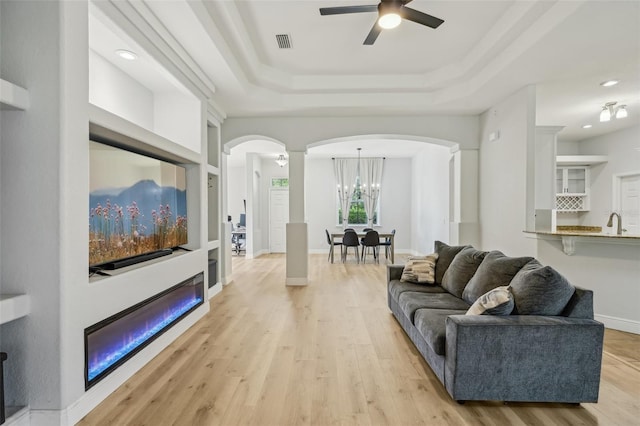707 9th Ave SW, Ruskin, FL 33570 - living area featuring arched walkways, a tray ceiling, ceiling fan, light wood-style flooring, and a chandelier