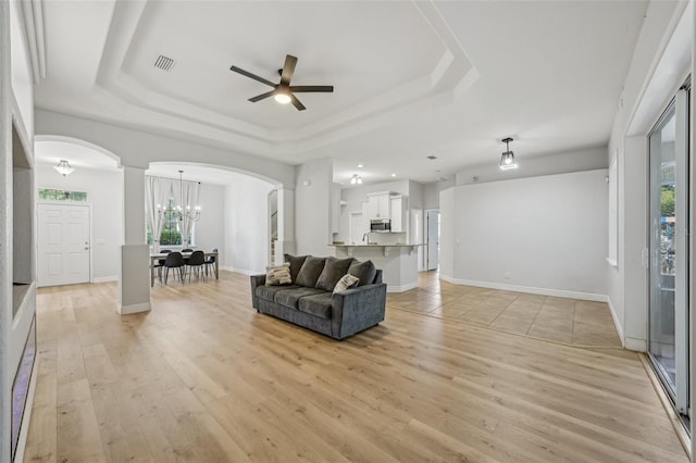 707 9th Ave SW, Ruskin, FL 33570 - living room with a tray ceiling, arched walkways, a ceiling fan, a chandelier, and light wood-style flooring