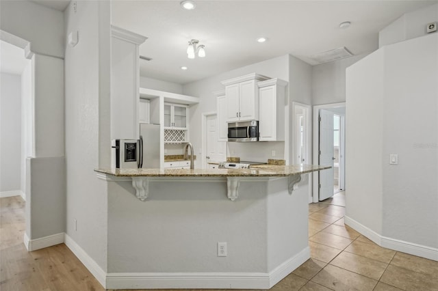 707 9th Ave SW, Ruskin, FL 33570 - kitchen with light stone counters, stainless steel appliances, a breakfast bar area, a peninsula, and white cabinetry