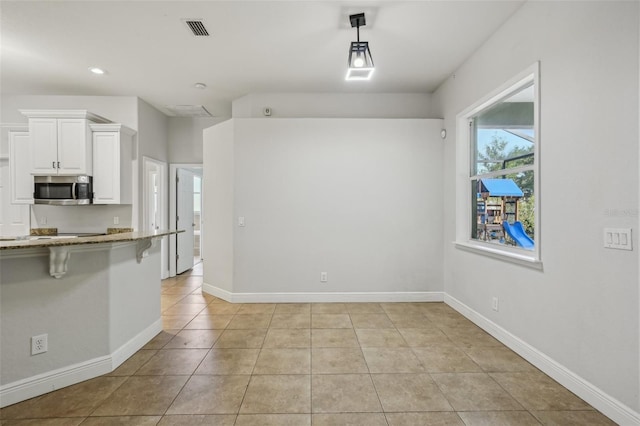 707 9th Ave SW, Ruskin, FL 33570 - kitchen featuring stainless steel microwave, light stone counters, white cabinetry, light tile patterned floors, and a breakfast bar