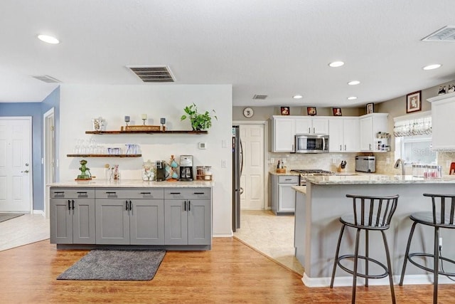 5525 Turtle Crossing Loop, Tampa, FL 33625 - kitchen with stainless steel appliances, gray cabinets, a kitchen bar, open shelves, and light wood-style floors