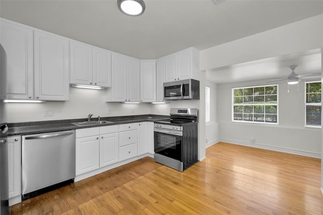5642 9th Ave N, Saint Petersburg, FL 33710 - kitchen featuring appliances with stainless steel finishes, a sink, light wood-style floors, white cabinets, and dark countertops