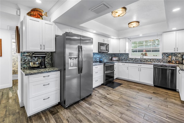 9611 107th Ave N, Largo, FL 33773 - kitchen featuring stainless steel appliances, a sink, a tray ceiling, wood finished floors, and backsplash