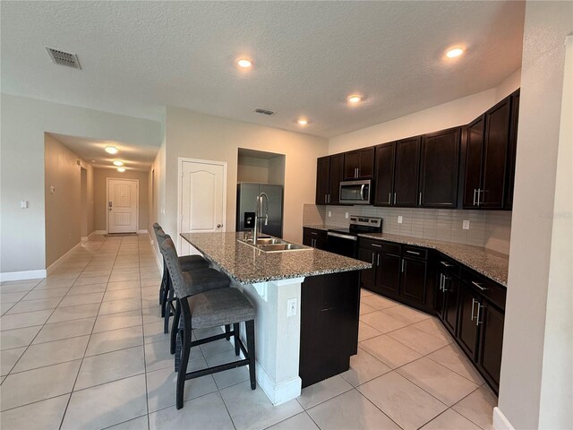 1509 Venice Ln, Davenport, FL 33896 - kitchen featuring appliances with stainless steel finishes, light tile patterned floors, a kitchen breakfast bar, tasteful backsplash, and a kitchen island with sink