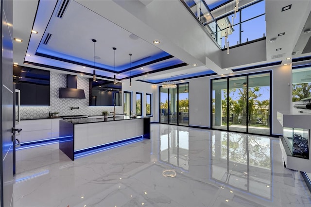 6530 Simone Shores Cir, Apollo Beach, FL 33572 - kitchen featuring modern cabinets, light marble finish floors, wall chimney range hood, a tray ceiling, and a towering ceiling