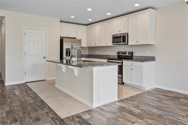 12170 Gothic Rd, Spring Hill, FL 34610 - kitchen featuring stainless steel appliances, a sink, white cabinets, an island with sink, and dark stone counters