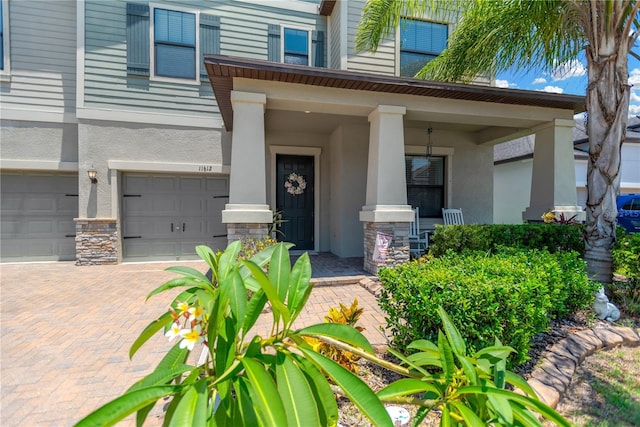 11612 Sunburst Marble Rd, Riverview, FL 33579 - view of exterior entry featuring stucco siding, an attached garage, stone siding, and covered porch
