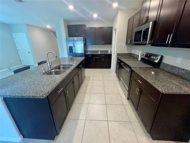 9520 Lemon Drop Loop, Sun City Center, FL 33573 - kitchen featuring stainless steel appliances, a sink, light tile patterned floors, dark stone countertops, and a center island with sink