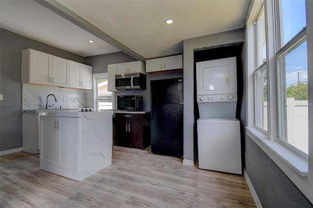 2627 17th Ave N, Saint Petersburg, FL 33713 - kitchen featuring stainless steel microwave, estacked washer and dryer, baseboards, white cabinets, and light wood-type flooring