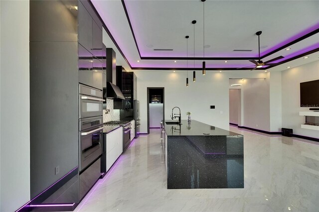 6532 Simone Shores Cir, Apollo Beach, FL 33572 - kitchen with a raised ceiling, modern cabinets, a sink, ceiling fan, and wall chimney exhaust hood