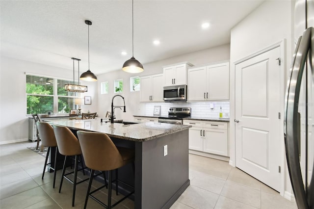 32825 Sand Creek Dr, Wesley Chapel, FL 33543 - kitchen featuring stainless steel appliances, a sink, decorative backsplash, a center island with sink, and white cabinets
