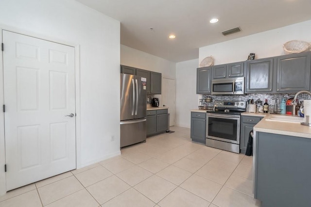15958 Marcello Cir, Naples, FL 34110 - kitchen with stainless steel appliances, a sink, gray cabinetry, light countertops, and decorative backsplash