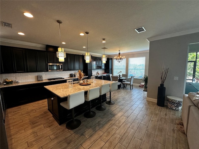 1521 Sourwood Dr, Ocoee, FL 34761 - kitchen with stainless steel microwave, dark cabinetry, a chandelier, ornamental molding, and a kitchen island with sink