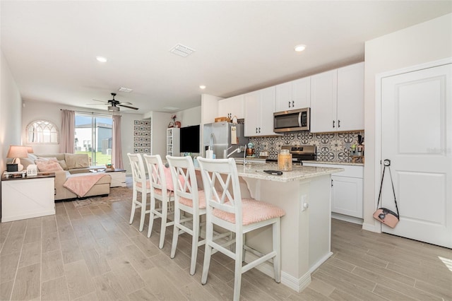 13958 Richland Gulf Cir, Parrish, FL 34219 - kitchen featuring appliances with stainless steel finishes, light wood-style floors, a breakfast bar area, ceiling fan, and a center island with sink