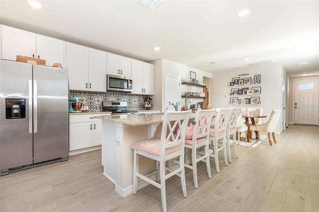13958 Richland Gulf Cir, Parrish, FL 34219 - kitchen with stainless steel appliances, light wood-style flooring, a kitchen island, decorative backsplash, and white cabinetry