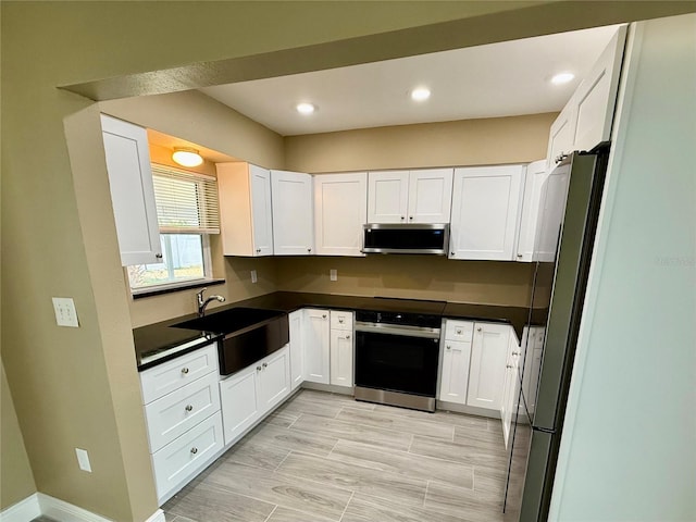 440 89th Ave, St Pete Beach, FL 33706 - kitchen with appliances with stainless steel finishes, a sink, dark countertops, white cabinetry, and recessed lighting