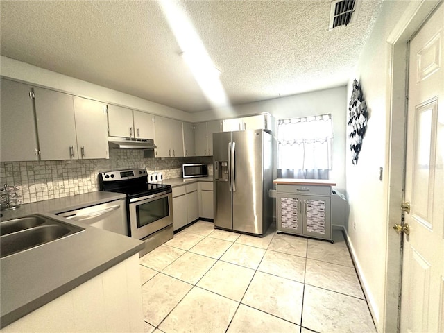 13100 Serpentine Dr, Hudson, FL 34667 - kitchen featuring appliances with stainless steel finishes, under cabinet range hood, dark countertops, backsplash, and light tile patterned flooring