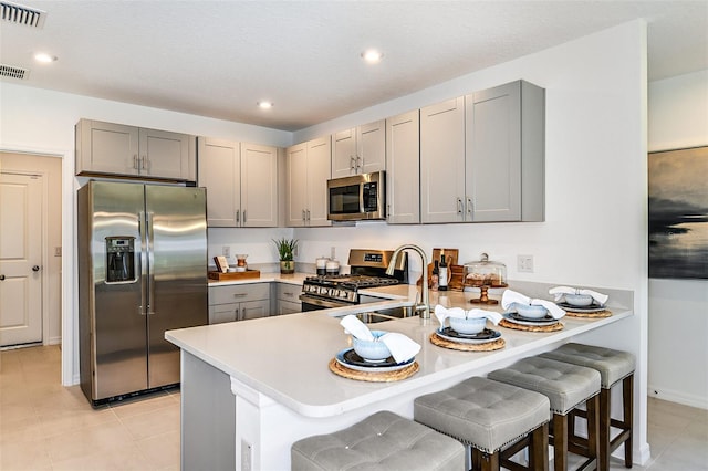 12435 Gust Ct, Hudson, FL 34669 - kitchen with stainless steel appliances, gray cabinetry, a peninsula, light tile patterned floors, and recessed lighting