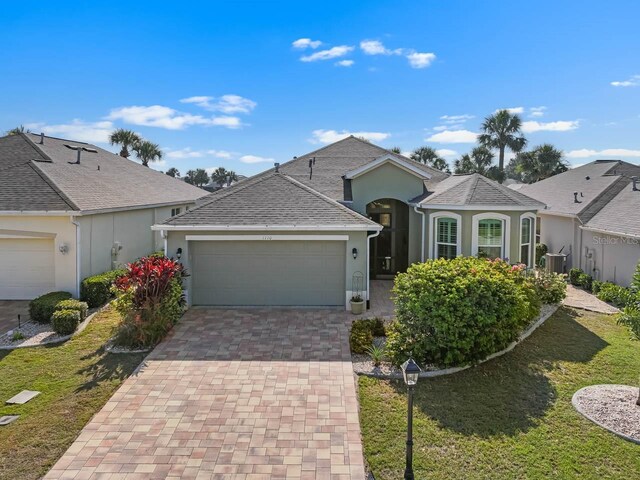 1110 Jasmine Creek Ct, Sun City Center, FL 33573 - view of front facade featuring stucco siding, a garage, decorative driveway, roof with shingles, and a front yard