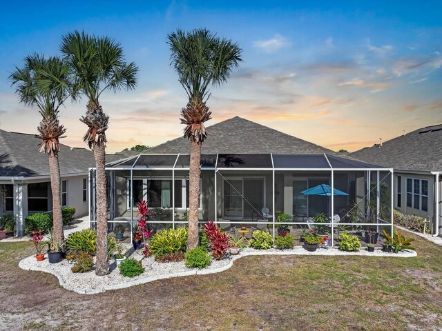 1110 Jasmine Creek Ct, Sun City Center, FL 33573 - back of house at dusk featuring a lawn, a shingled roof, and glass enclosure