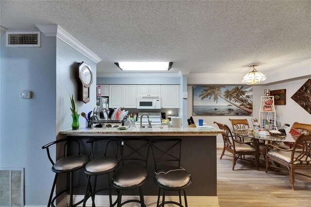 9481 Highland Oak Dr Unit 1511, Tampa, FL 33647 - kitchen featuring white microwave, a textured ceiling, crown molding, a peninsula, and a breakfast bar area