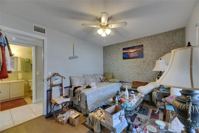 9481 Highland Oak Dr Unit 1511, Tampa, FL 33647 - bedroom with wallpapered walls, connected bathroom, light wood-style flooring, a textured ceiling, and ceiling fan