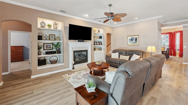 5704 Eaglemount Cir, Lithia, FL 33547 - living area with arched walkways, a ceiling fan, light wood-style floors, a tile fireplace, and crown molding