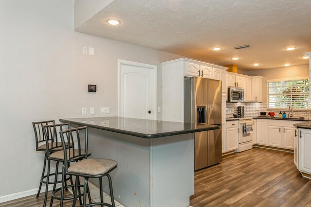 4021 Vana Dr, Sarasota, FL 34241 - kitchen featuring appliances with stainless steel finishes, dark wood-style floors, a peninsula, a sink, and a breakfast bar area