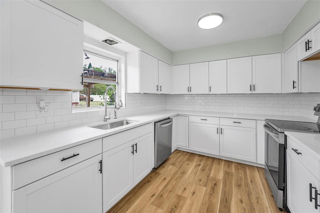 1412 Coburn Dr, Tarpon Springs, FL 34689 - kitchen featuring appliances with stainless steel finishes, a sink, white cabinets, light countertops, and light wood-style flooring