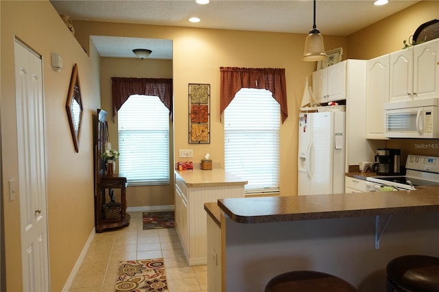311 Kelsey Way Unit 3, Sun City Center, FL 33573 - kitchen with white appliances, a breakfast bar area, dark countertops, light tile patterned floors, and white cabinetry