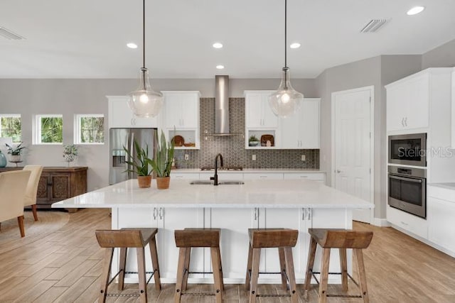 14223 Lambert Bridge Ln, Lithia, FL 33547 - kitchen with wall chimney range hood, appliances with stainless steel finishes, light wood-style flooring, a kitchen bar, and recessed lighting