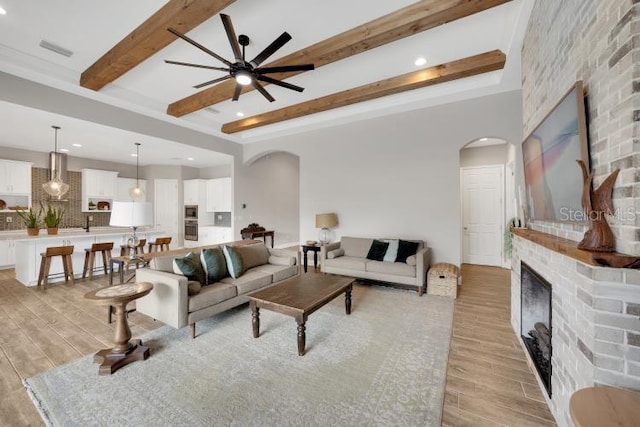 14223 Lambert Bridge Ln, Lithia, FL 33547 - living area featuring arched walkways, light wood finished floors, beamed ceiling, a fireplace, and ceiling fan