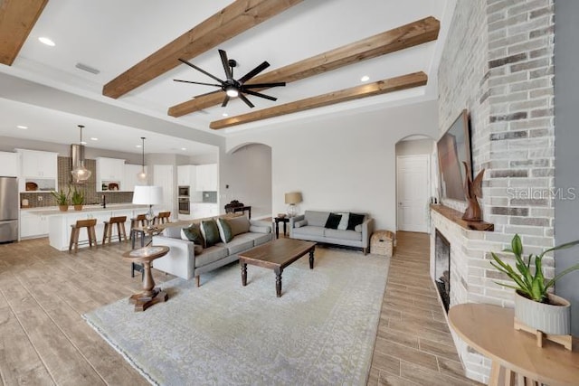 14223 Lambert Bridge Ln, Lithia, FL 33547 - living room with arched walkways, light wood finished floors, beamed ceiling, a ceiling fan, and a fireplace