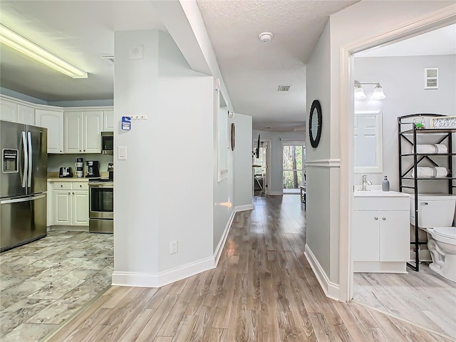 hall featuring light wood finished floors, baseboards, and a sink