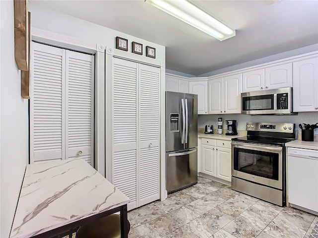 kitchen with appliances with stainless steel finishes, white cabinets, light stone counters, and light marble finish floors