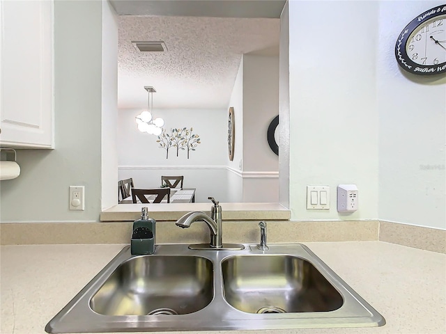 kitchen featuring a sink, a textured ceiling, light countertops, and white cabinetry