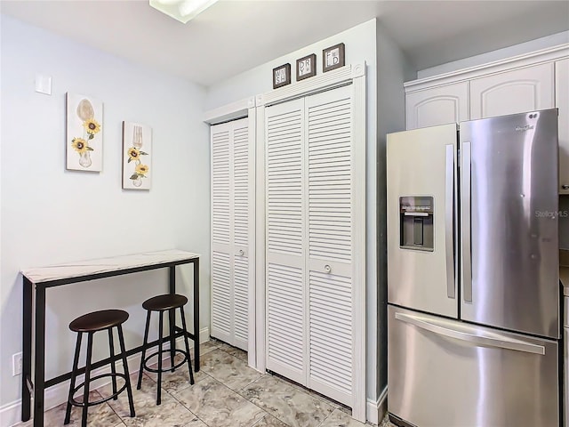 kitchen with stainless steel fridge, a kitchen breakfast bar, and light stone counters