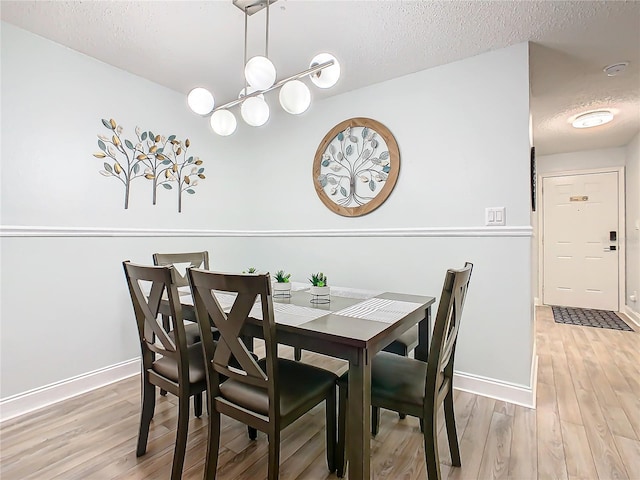 dining space with a textured ceiling, baseboards, light wood-style floors, and a chandelier