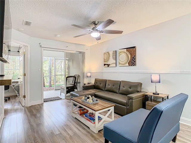 living room with a textured ceiling, a ceiling fan, light wood-style flooring, and baseboards
