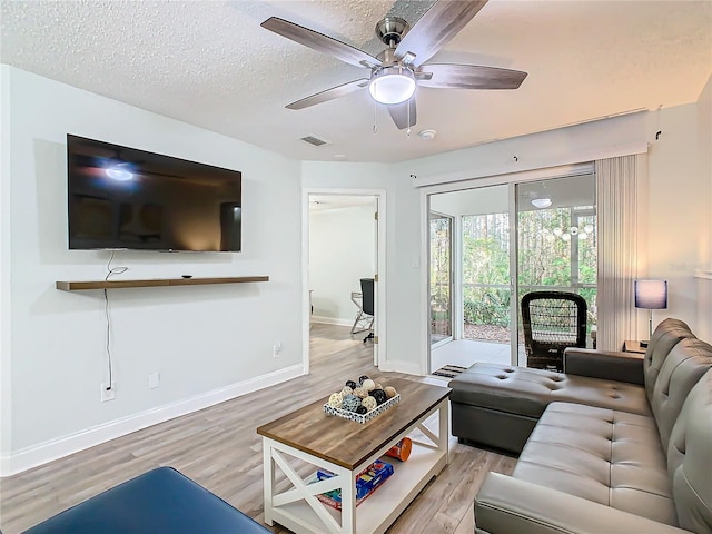 living room featuring light wood-style floors, ceiling fan, baseboards, and a textured ceiling