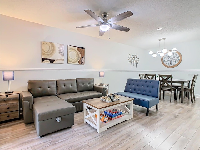 living room with light wood-style flooring, a ceiling fan, a chandelier, and a textured ceiling