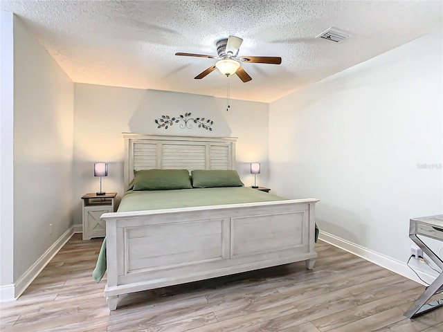bedroom with a textured ceiling, light wood finished floors, baseboards, and a ceiling fan