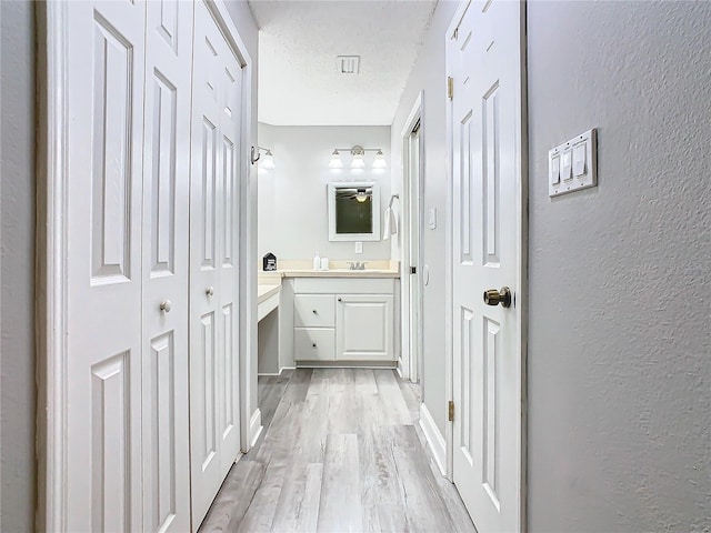bathroom with a closet, vanity, wood finished floors, a textured ceiling, and a textured wall