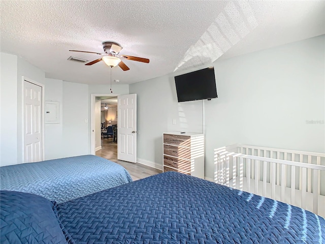 bedroom with a textured ceiling, wood finished floors, ceiling fan, baseboards, and electric panel